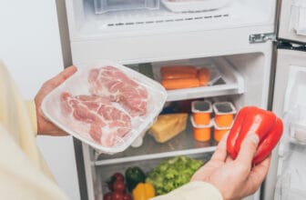 男性手拿冷凍肉與甜椒站在裝滿食物的冰箱前 / Man holding frozen meat and bell pepper near an open well-stocked fridge